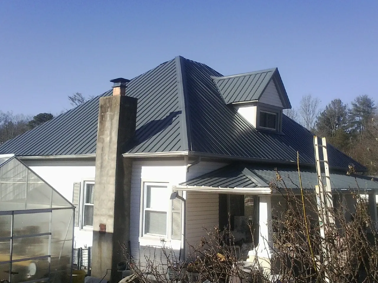 Dark blue standing seam metal roof on a white farmhouse with dormer — Slate & Tile Roof Repair by Roofing Brothers in Grenada