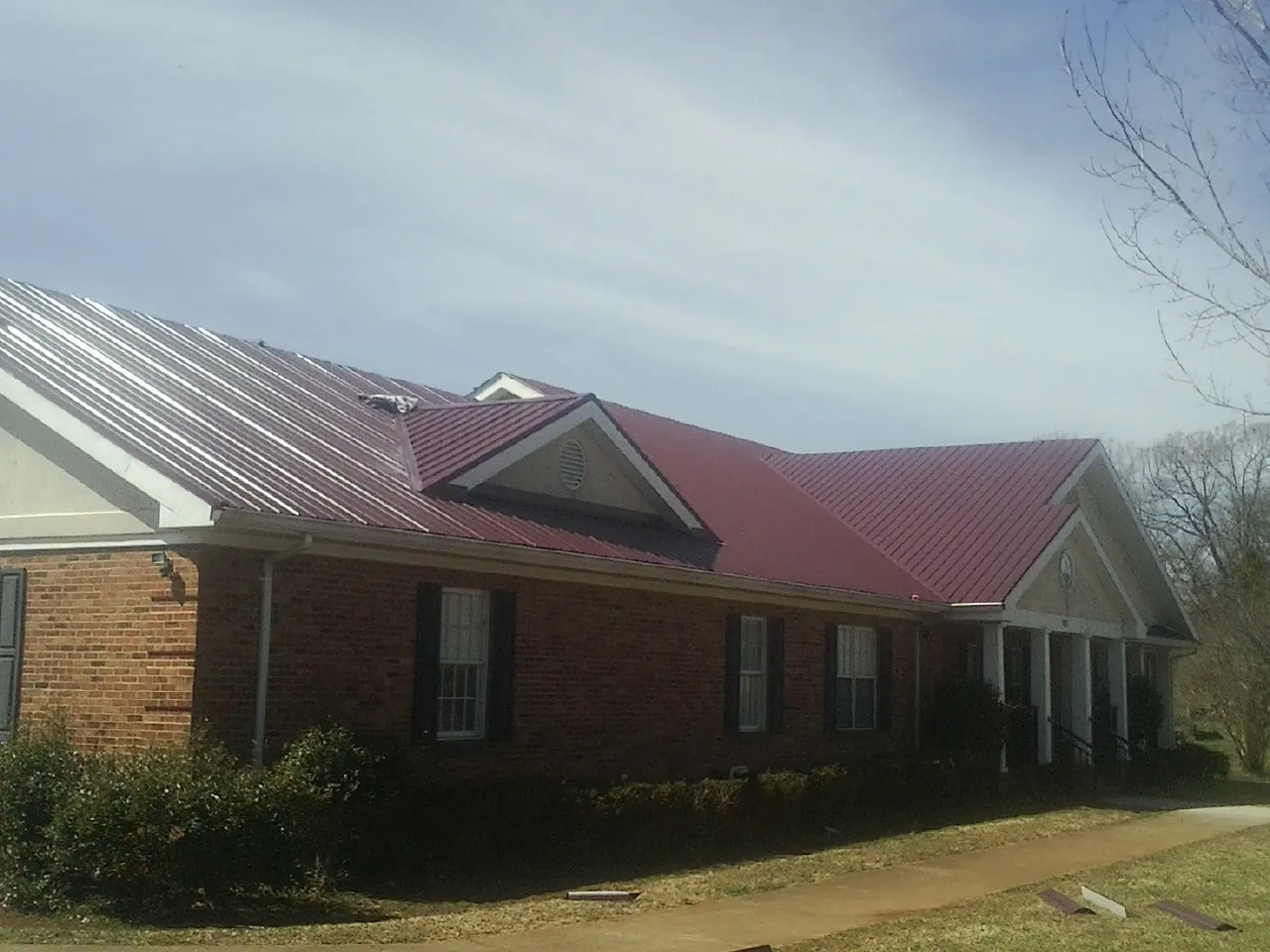 Red metal roof with gabled entries on a long brick building, from a Hail Damage Roof Repair job in Grenada