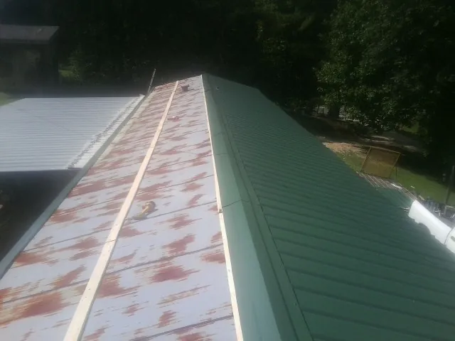 Old rusted panels beside newly installed green metal roofing — Wind Damage Roof Repair by Roofing Brothers in Grenada