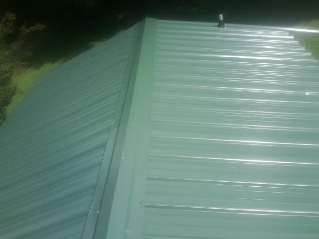 New green metal panels meeting at the ridge of a roof — Flat Roof Repair work by our crew in Grenada