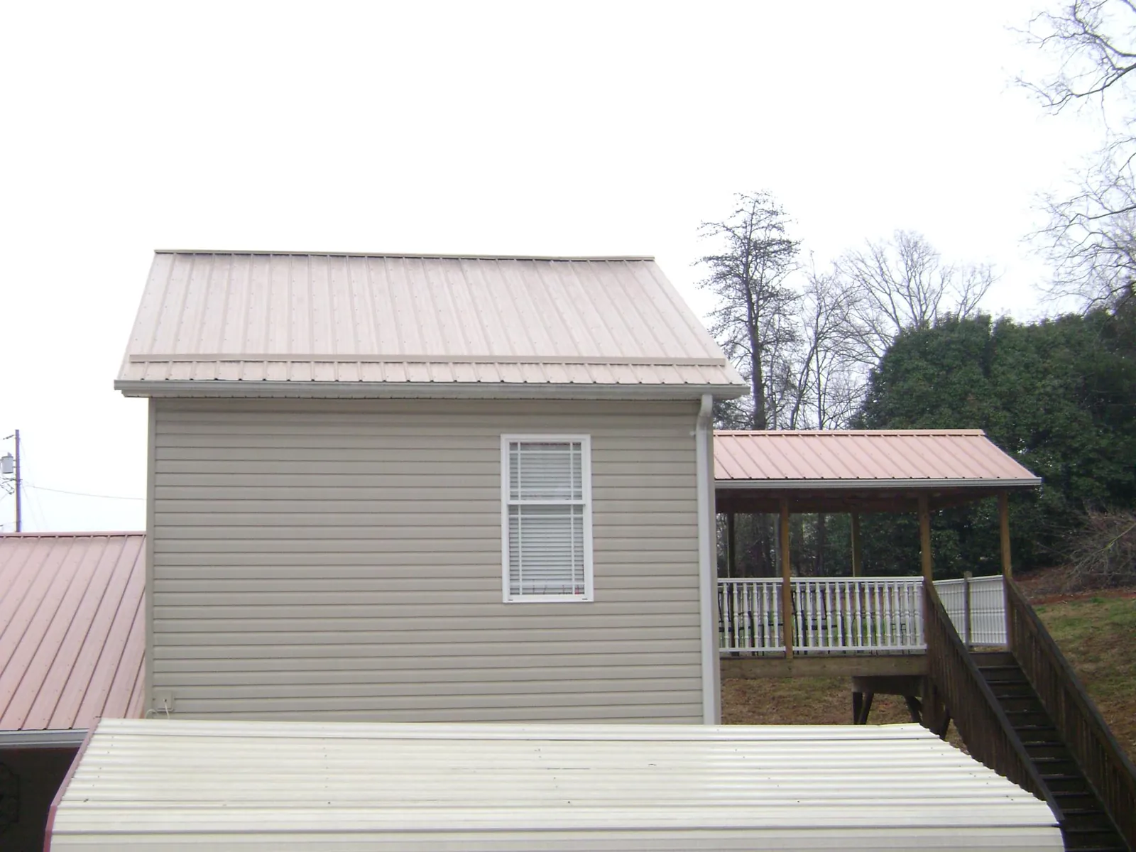 Tan metal roofs on a two story addition and attached porch, from a Roof Replacement job in Grenada